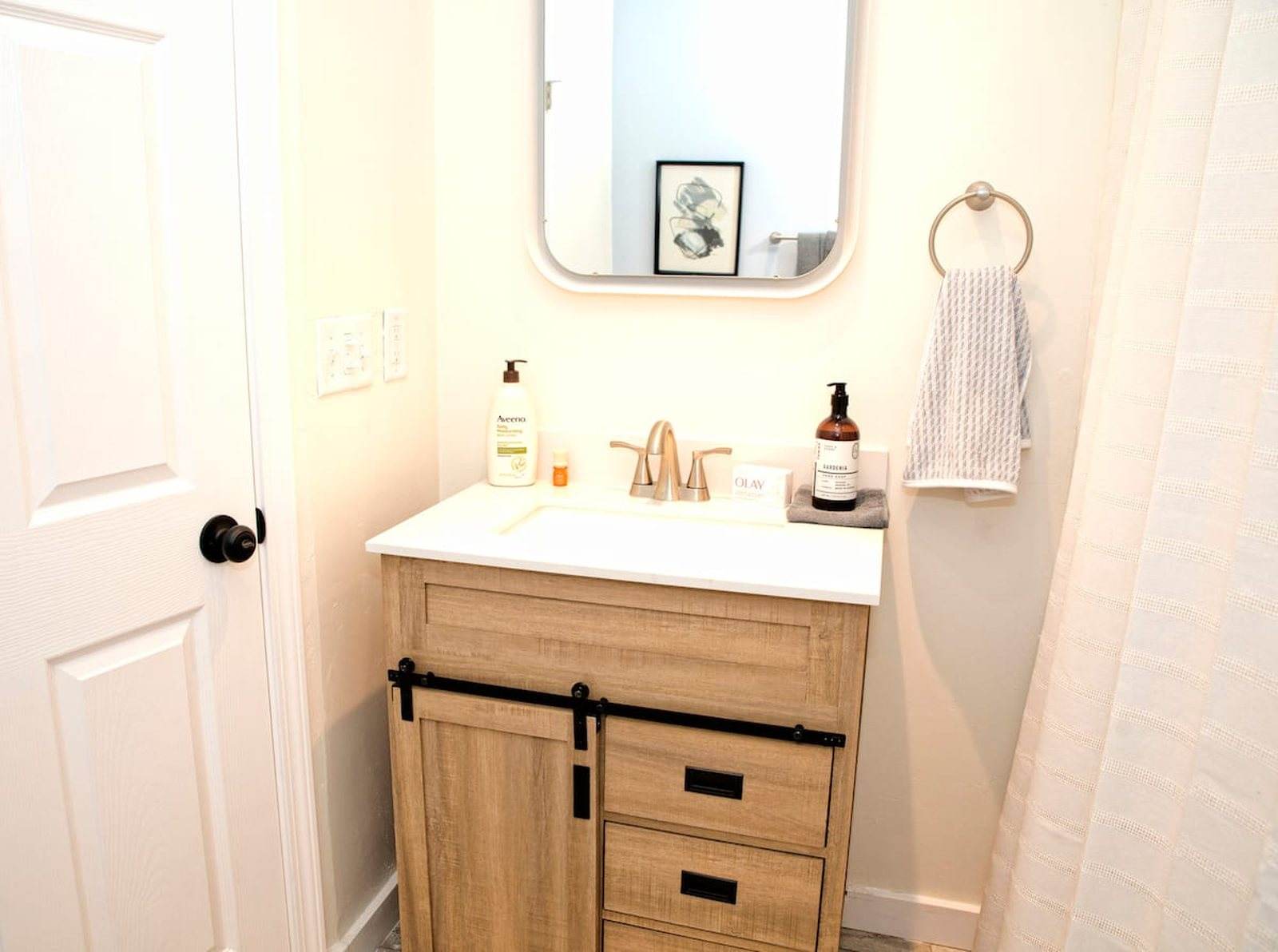 Completed bathroom with a timber vanity, white counter, rounded mirror and black hardware.