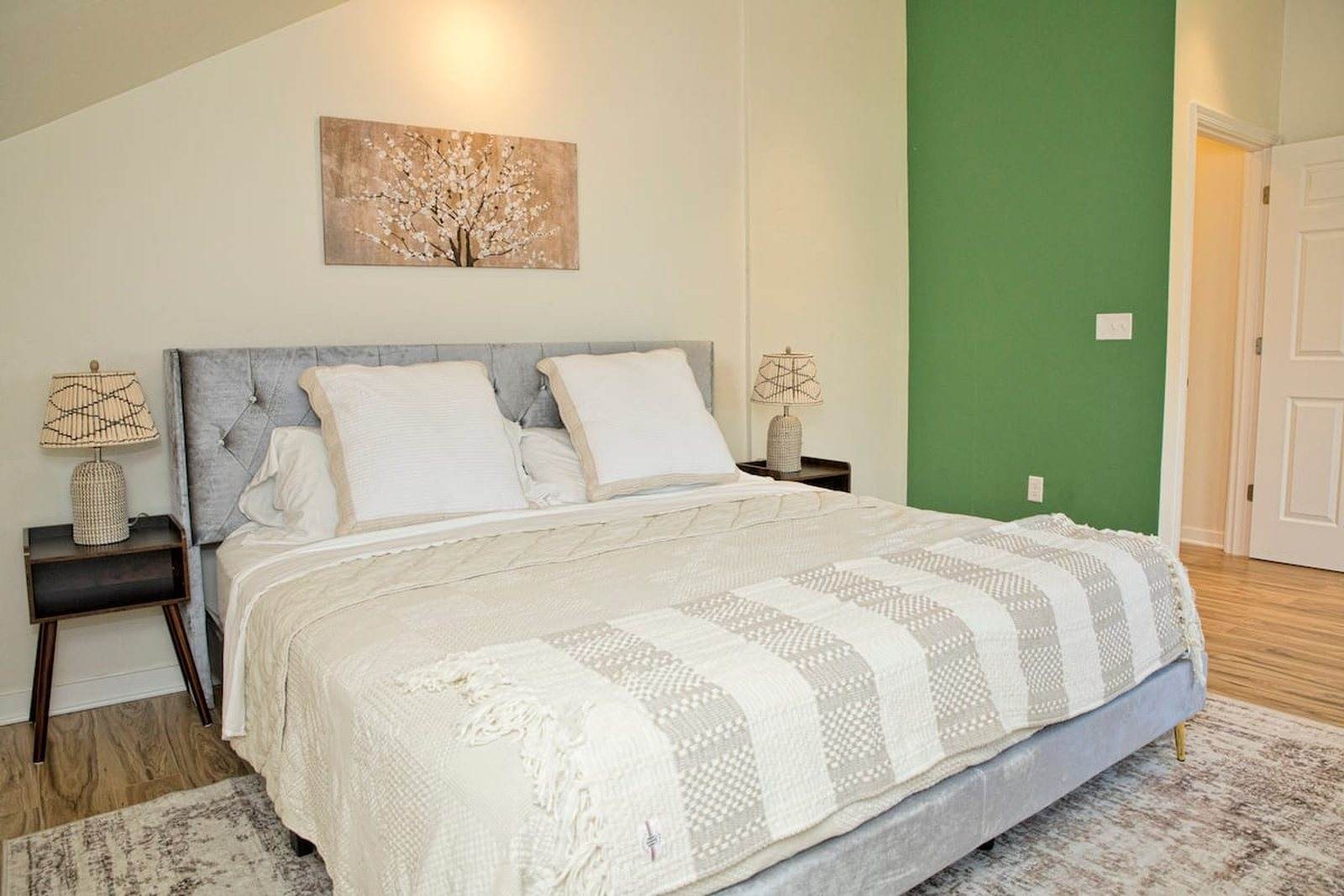 Completed bedroom with a light upholstered bed, timber floor and a green accent wall.