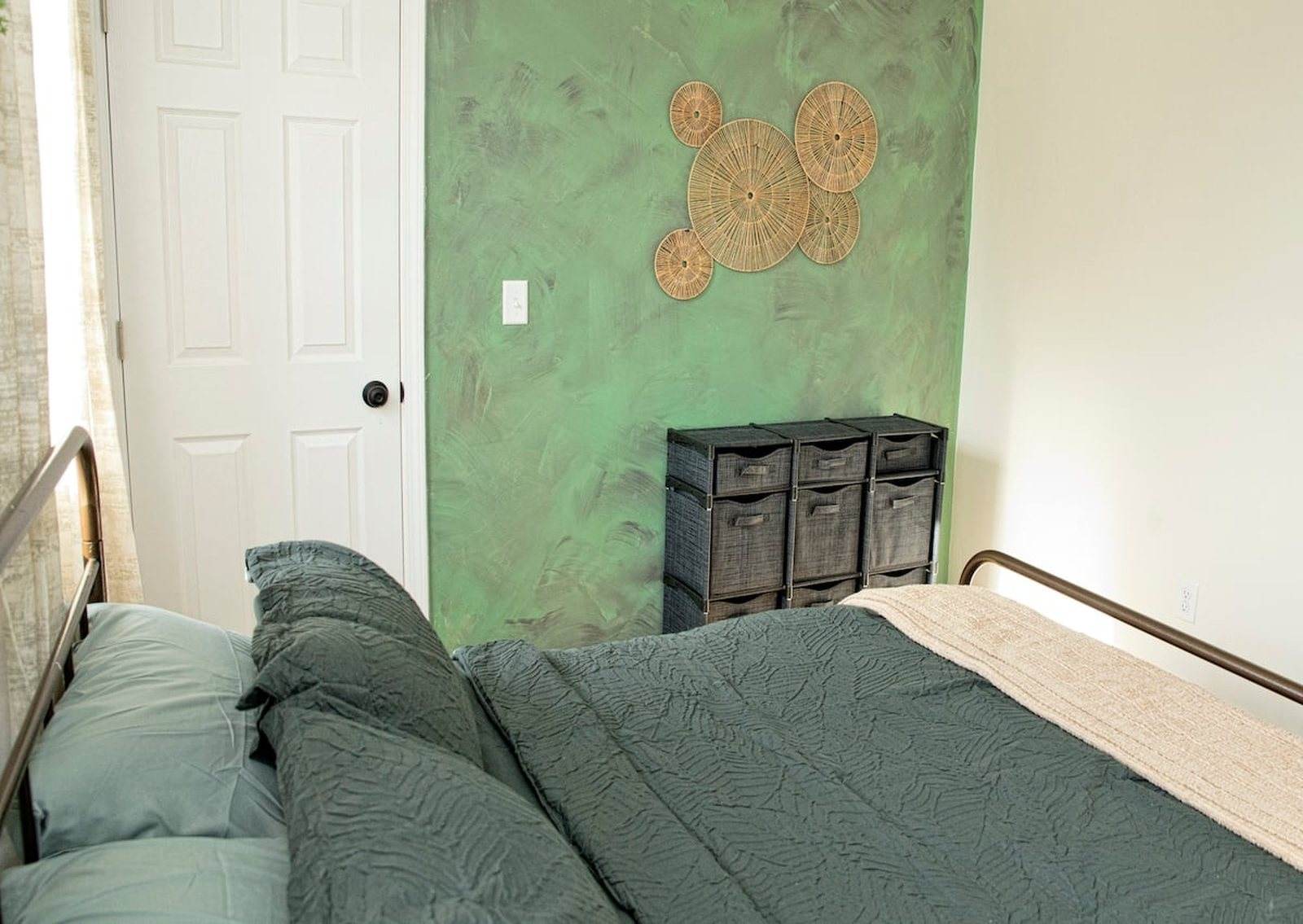 Completed bedroom with a green bedspread, pale walls and a green accent wall.