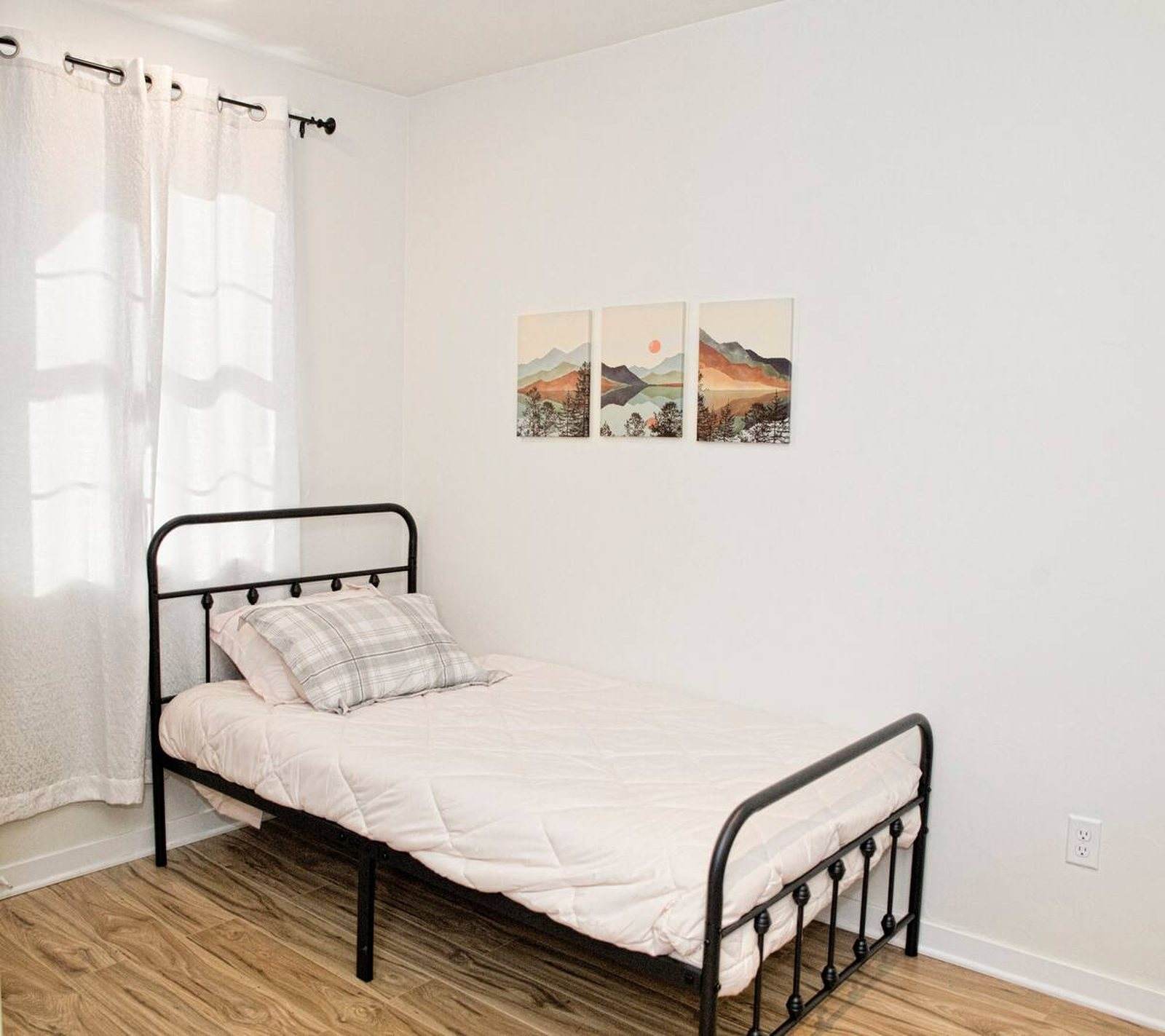 Completed bedroom with a black metal bed, timber floor and soft natural light.