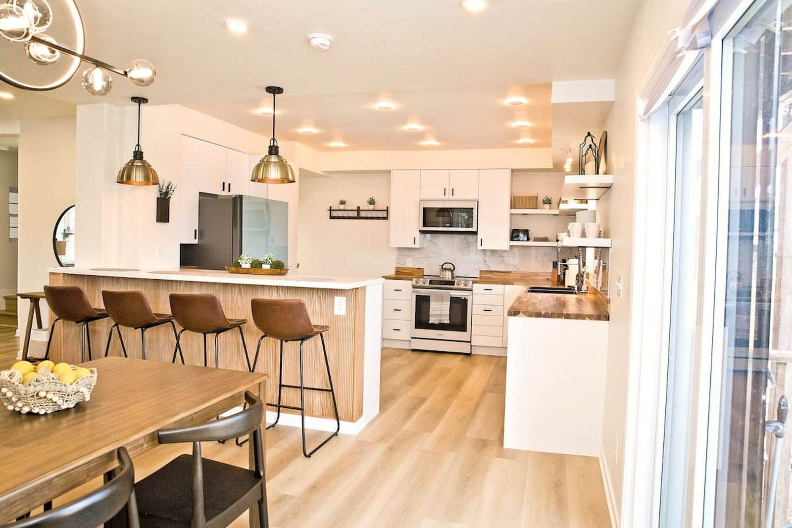 Completed dining area looking into the white kitchen with a wide island and wood counters.