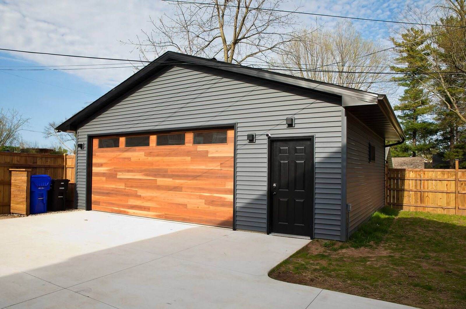 Completed detached garage with grey siding, black trim, a timber overhead door and a concrete apron.