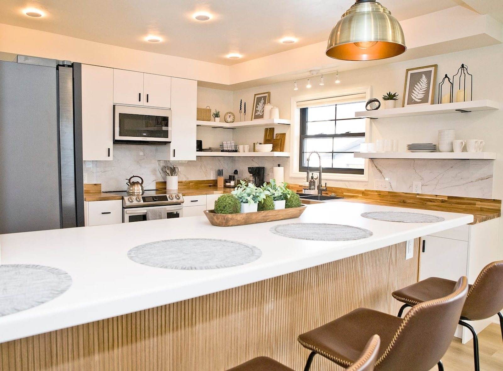 Completed kitchen with a long white island, wood-front detail, white cabinets and pendant lighting.