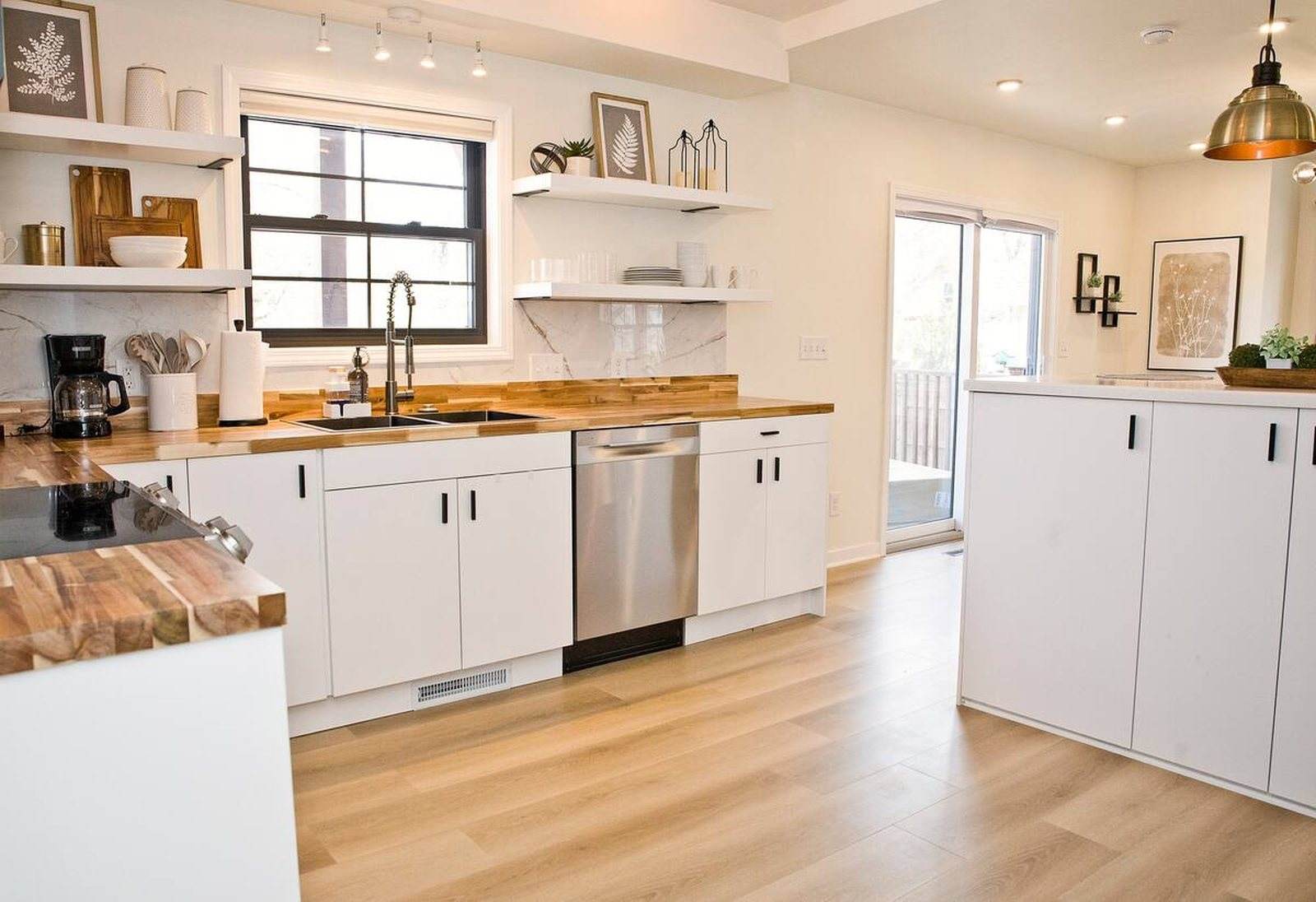 Completed kitchen with white cabinets, wood counters, open shelving and black-framed windows.