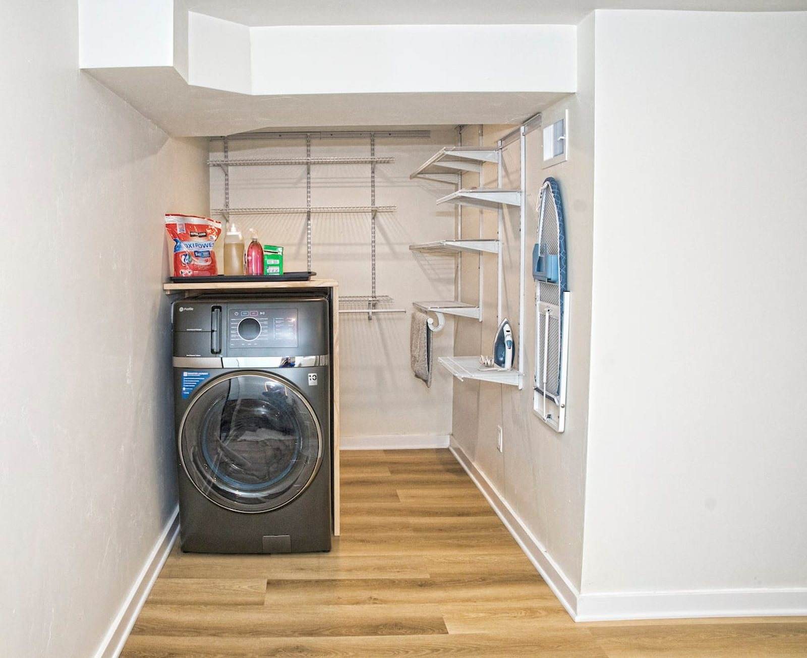 Completed laundry area with a front-loading washer, wall storage and a timber-look floor.