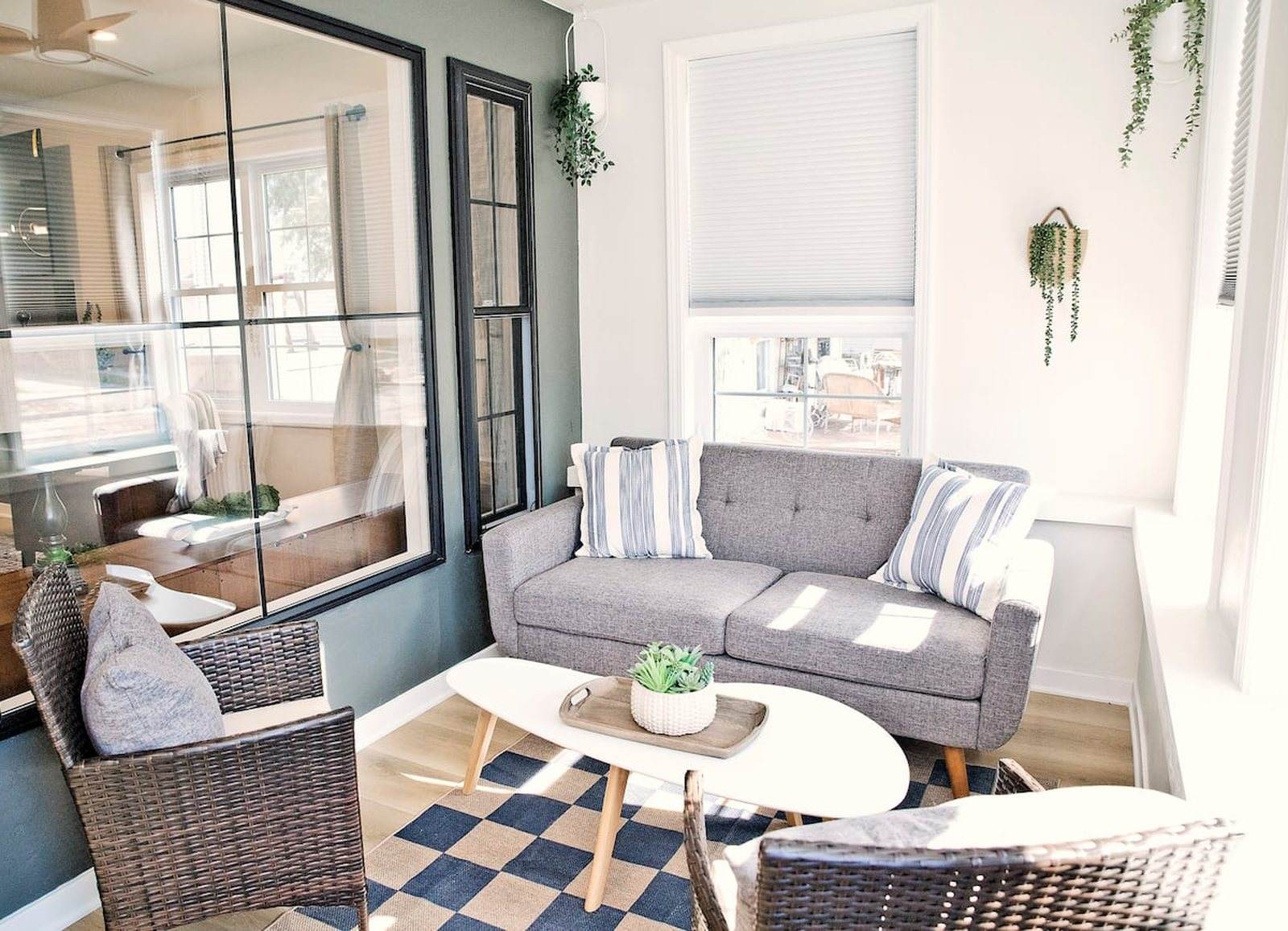 Completed sunroom with black-framed interior windows, pale walls and woven seating.