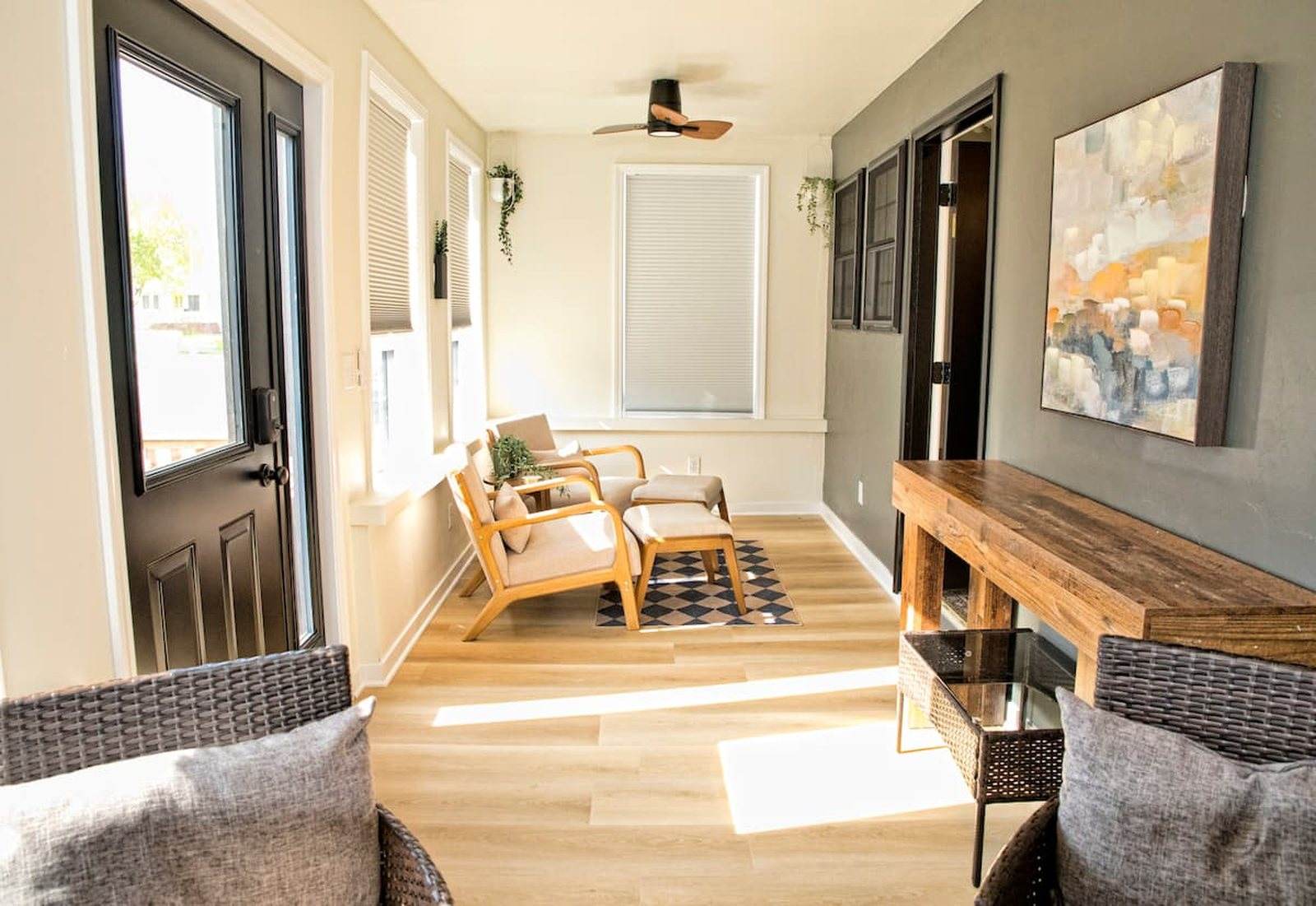 Completed sunroom seen from the opposite end, with woven seating, a sofa and a timber console beneath the windows.
