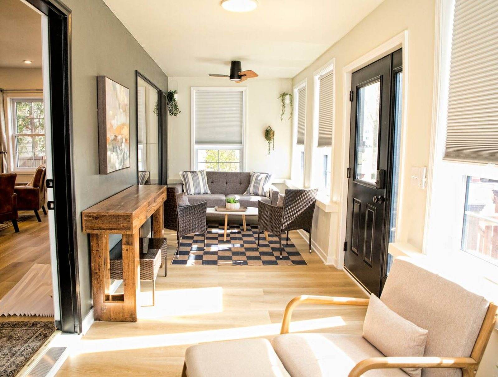 Completed long sunroom with black-framed windows, woven chairs, a pale sofa and daylight from both sides.