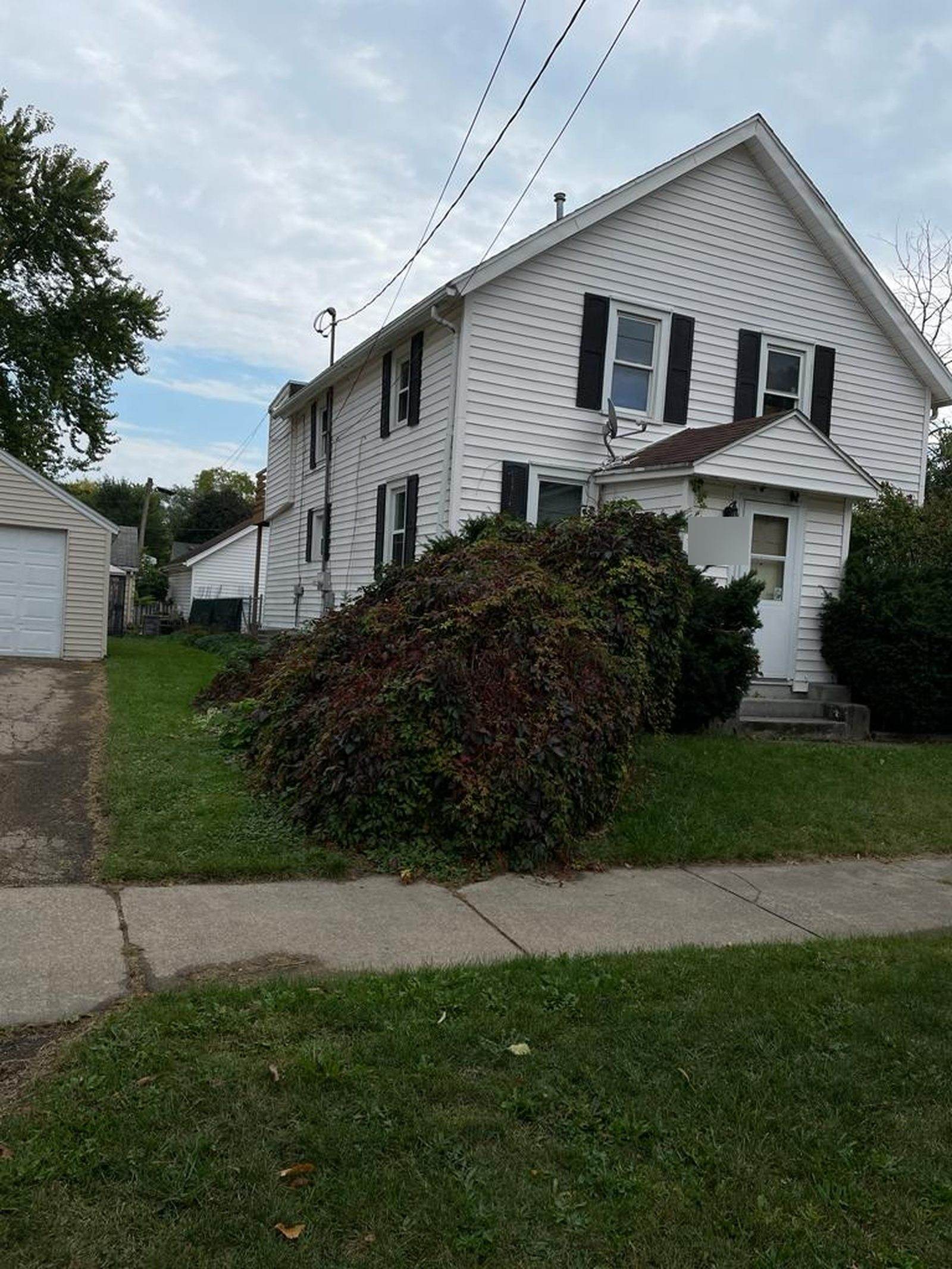 Before: white-sided Appleton duplex with black shutters, a small enclosed entrance and shrubs across the front.