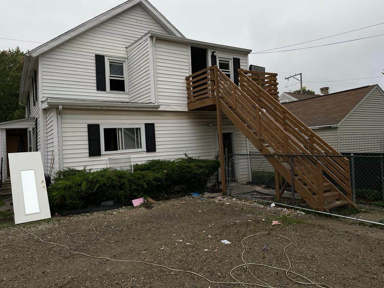 Before: rear of the white-sided duplex with an exterior timber stair and unfinished ground.