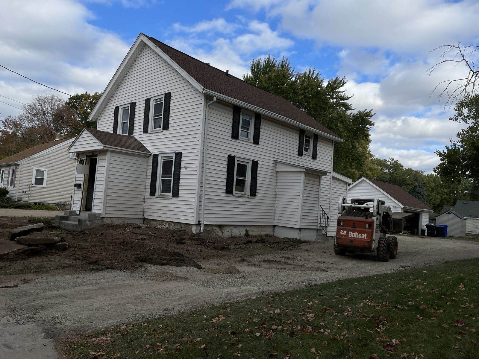 During construction: white-sided duplex beside an unfinished driveway, with a skid-steer and disturbed soil.