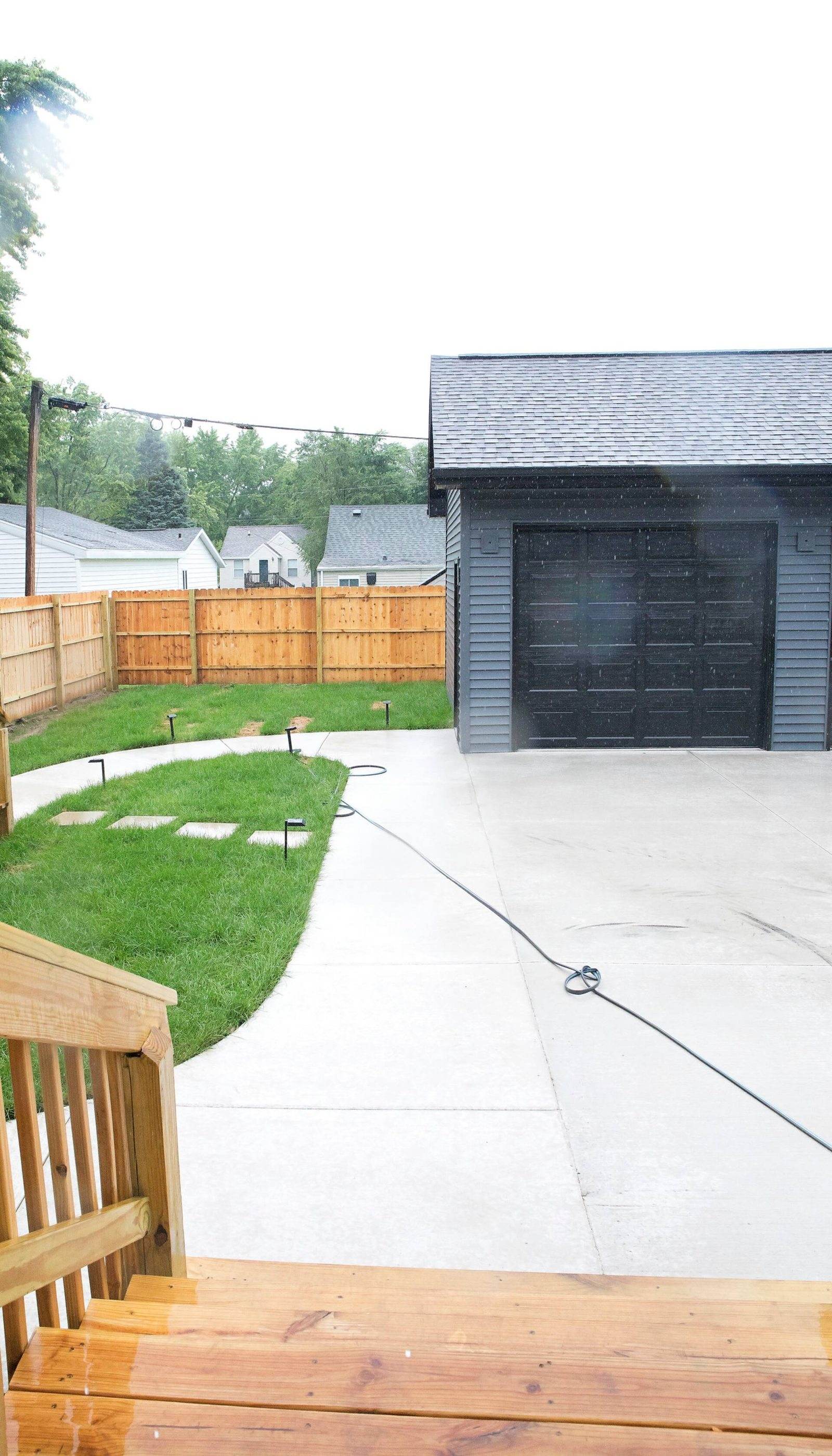 After: concrete driveway and curved walkway beside a dark-sided garage and timber privacy fence.