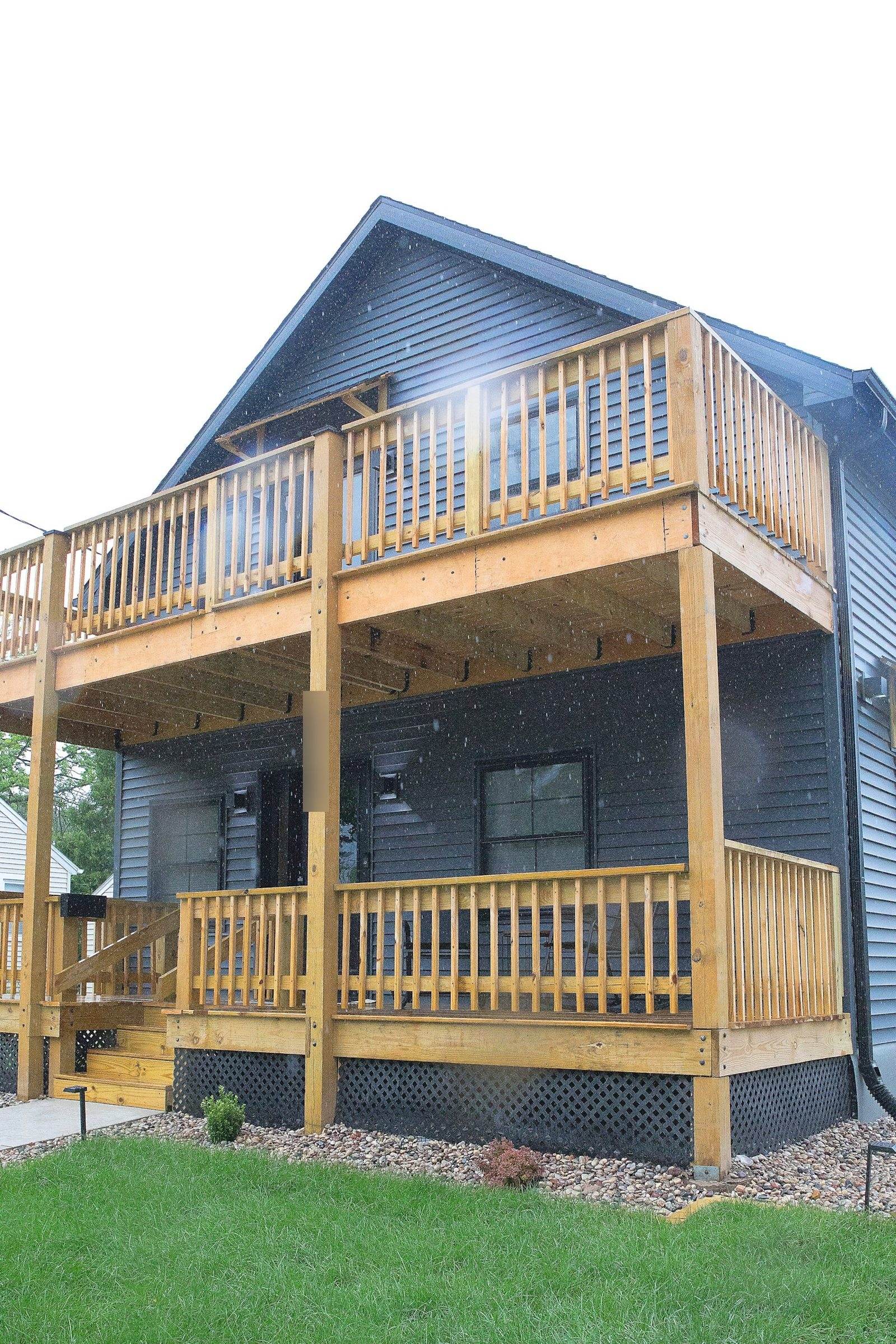 After: angled view of two-level timber front porch, dark siding and stone planting border.