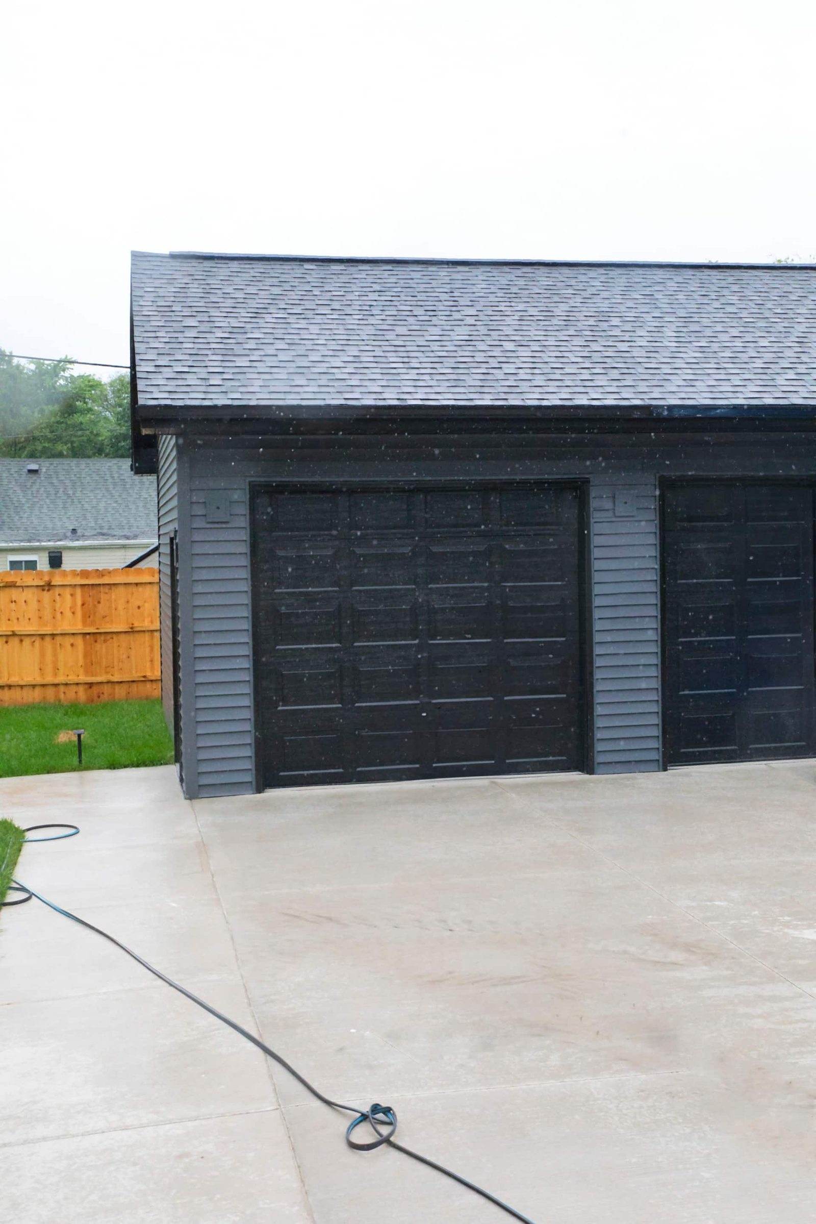 After: detached garage with dark siding, two dark overhead doors and a concrete apron.