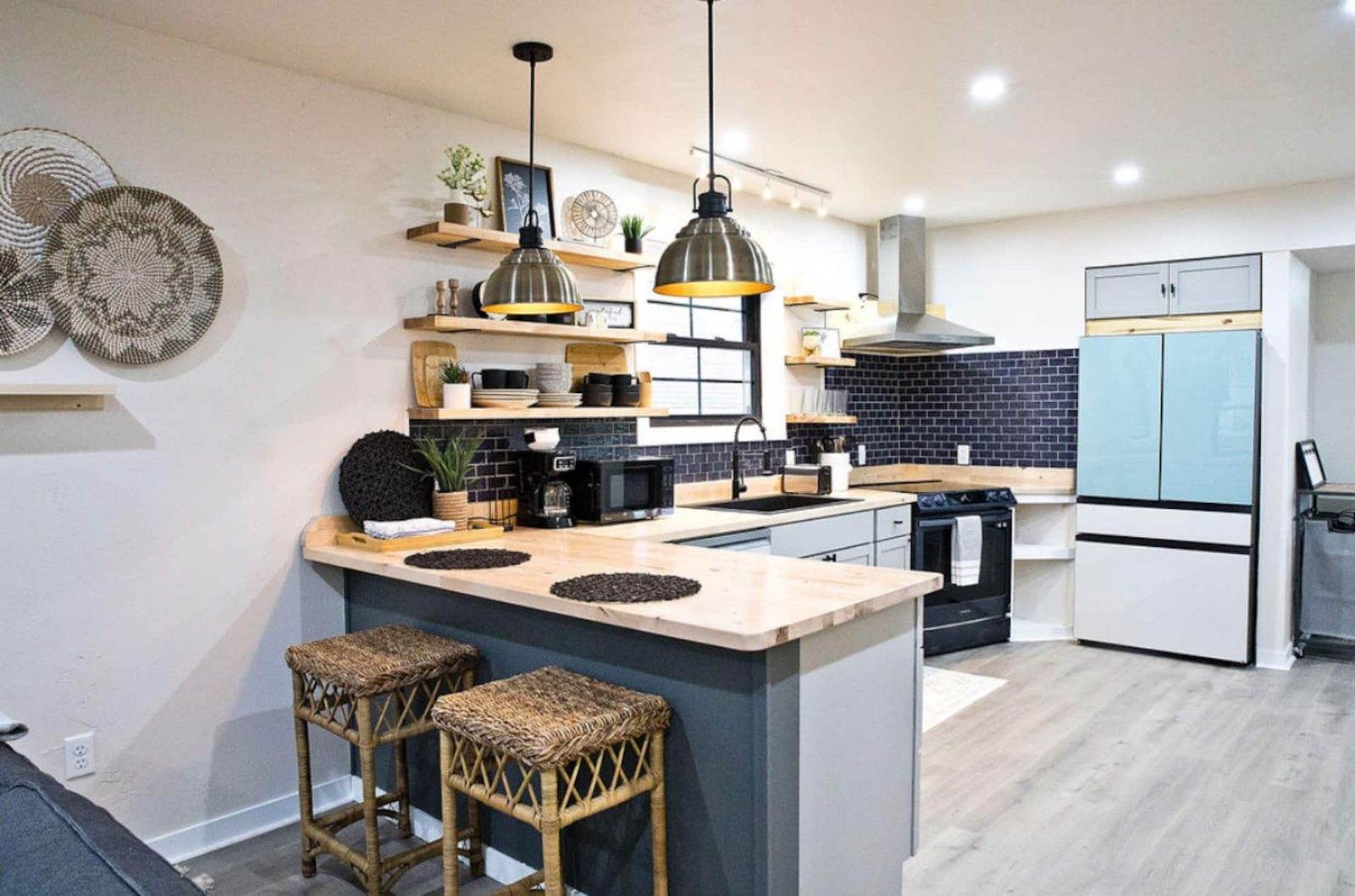 After: lower kitchen with timber counters, dark cabinets, black tile backsplash and pendant lights.