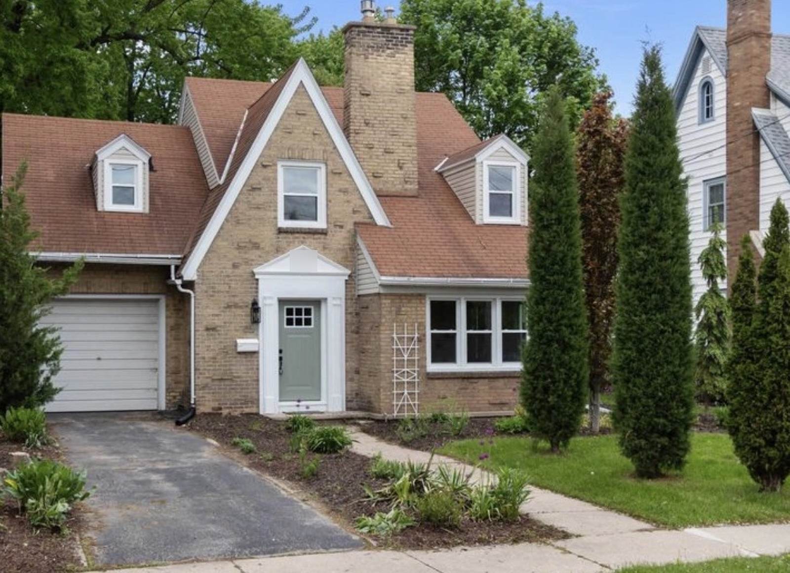 Before: Neenah house with unpainted brick, a white garage door, asphalt driveway and a narrow front path.