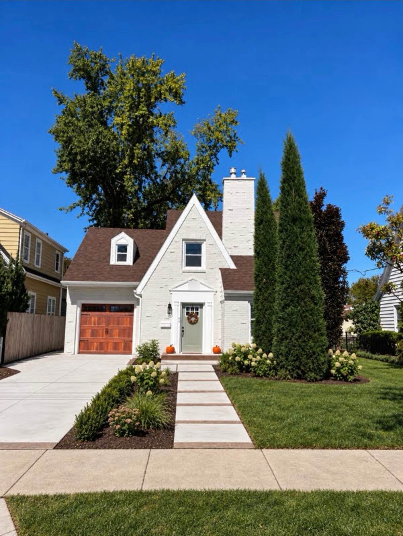 Completed Neenah exterior with painted white brick, a timber garage door, concrete driveway and walkway, green lawn and landscaped beds.