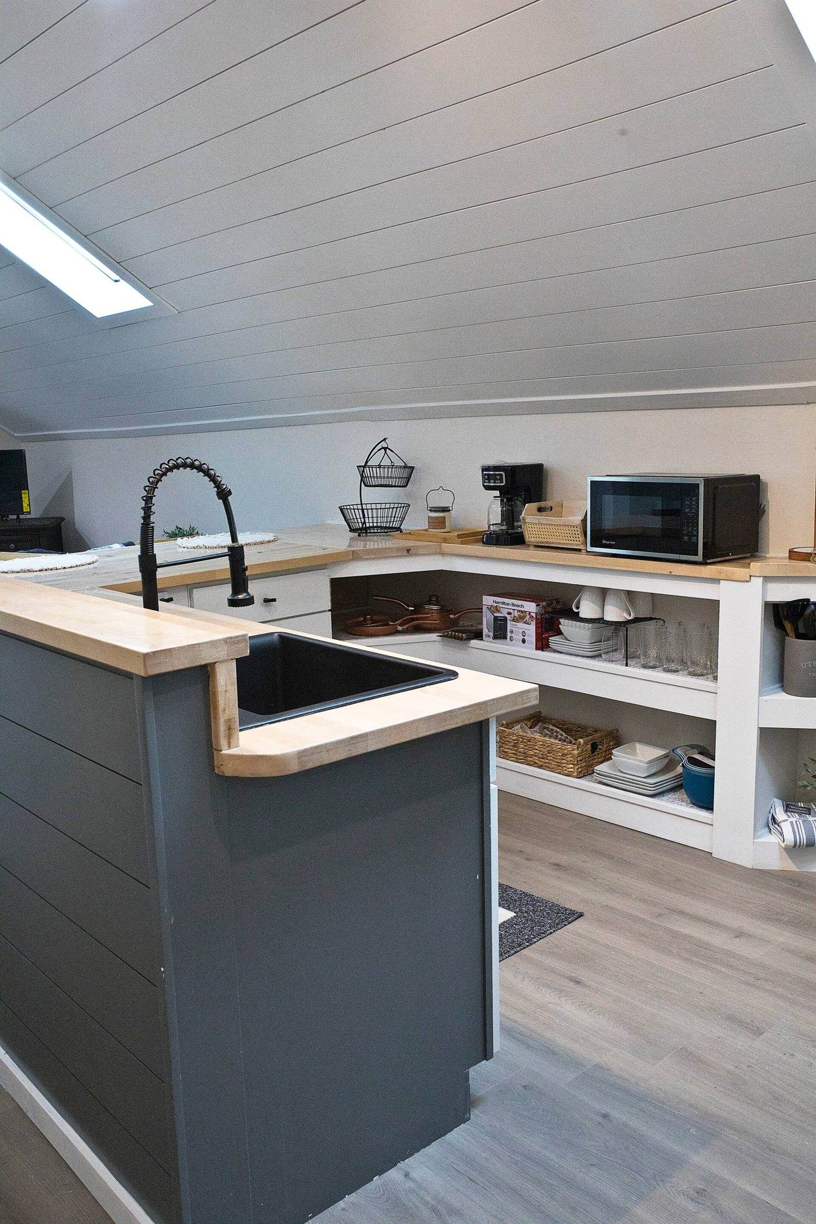 After: upper kitchen with pale timber counters, dark lower cabinets and a black faucet.